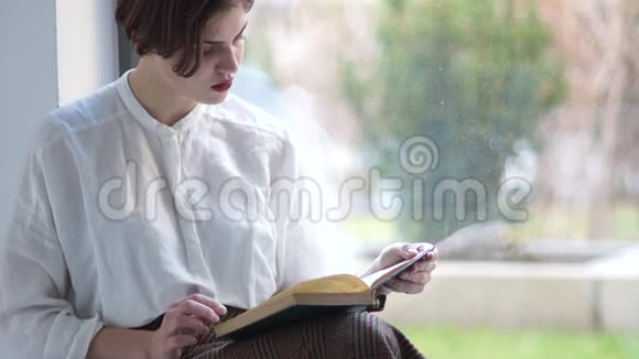 可爱的少年女孩坐在房子的窗户上读一本旧书快乐的女人视频的预览图
