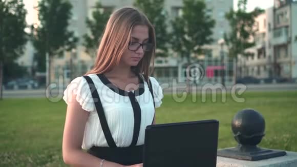 商务女性穿着白色衬衫和眼镜坐在街上的长凳上在笔记本电脑后面工作女孩累了视频的预览图