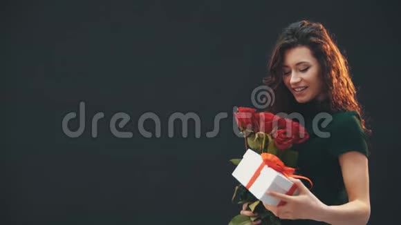 美丽的卷发黑发女孩站着欣赏着红色条纹和白色盒子绑在一起的红色玫瑰花束视频的预览图