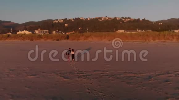 日落时分一对幸福的夫妇在雄伟的俄勒冈州海滩上一起跑步视频的预览图