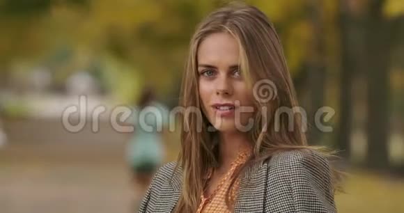 美丽的高加索女人站在秋天的公园里微笑着对着镜头一位迷人的神秘女孩视频的预览图