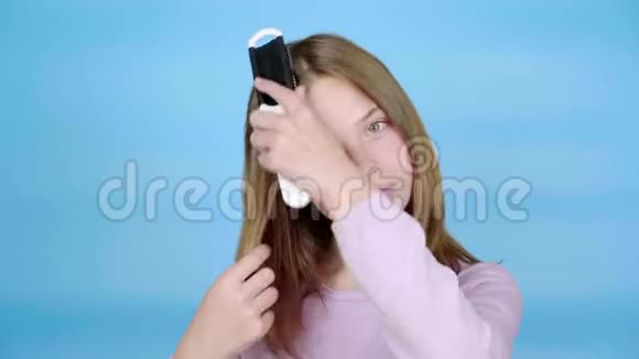 穿着粉红色套头衫的少女正用梳子梳头看着相机微笑着视频的预览图