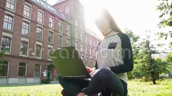 美丽而现代的女学生或自由职业者在笔记本电脑上工作坐在校园绿色草坪上的公园里集中注意力视频的预览图
