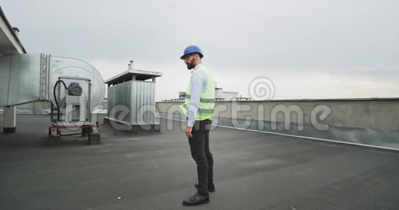 在建筑工地的屋顶上戴着头盔蓄着胡须的激动的建筑师翩翩起舞视频的预览图