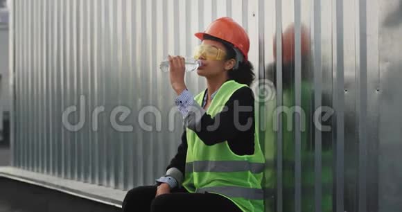 有魅力的非洲女工程师微笑着可爱地在建筑工地的屋顶上喝点水她的背景是她视频的预览图