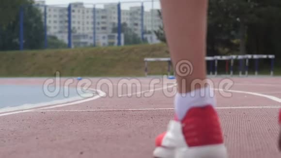 一名年轻女子运动员在慢动作训练中开始在城市田径跑道上奔跑的红色短腿视频的预览图