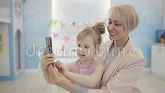 成年妇女和她的小女儿正在用智能手机进行视频翻译并挥舞着相机视频的预览图