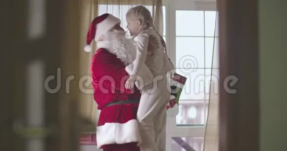 穿着圣诞老人服装抱着可爱白种人孩子的快乐白种人的肖像穿着睡衣的微笑女孩视频的预览图