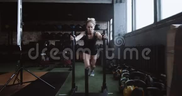 动机概念年轻的运动金发女子推动沉重的训练雪橇转向相机训练在健身房慢动作视频的预览图