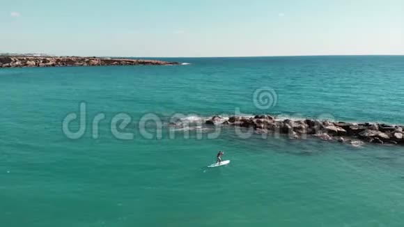 无人机在美丽的岩石海岸附近飞行年轻运动男子的鸟瞰可爱的男孩漂浮在岩石上奥视频的预览图