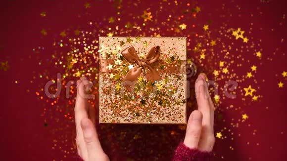 女人手打开礼盒闪耀着金色的星星闪闪发光的纸屑在红色背景下打开包装礼物视频的预览图