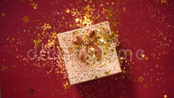 闪闪发光的金色星星红色背景上的礼品盒上闪闪发光的纸屑上景圣诞节和新年的纹理销售视频的预览图