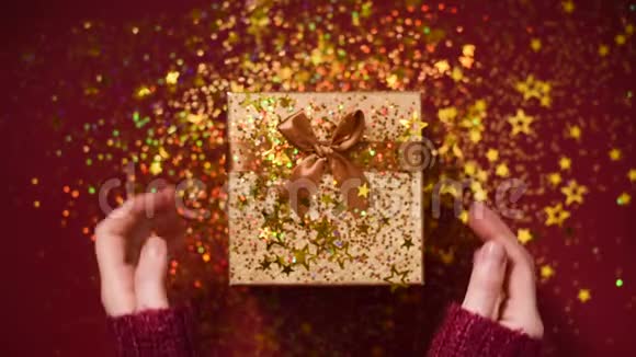 女人手打开礼盒闪耀着金色的星星闪闪发光的纸屑在红色背景下打开包装礼物视频的预览图