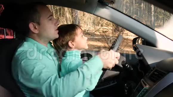 一个人转动汽车的车轮把他的儿子放在膝上快乐的父亲和他的孩子一起坐车旅行视频的预览图