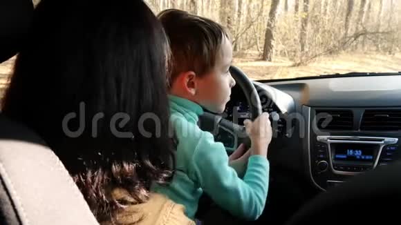 一个女人开车时把她的孩子抱在膝盖上一位母亲和儿子在司机里玩那个男孩转过身来视频的预览图