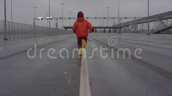 小男孩穿着黄色的橡胶靴沿着灰色的宽阔道路奔跑视频的预览图