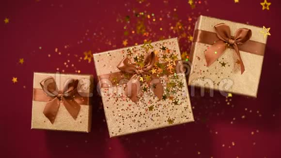 闪闪发光的金色星星红色背景上的礼品盒上闪闪发光的纸屑上景圣诞节和新年的纹理销售视频的预览图