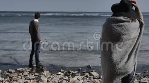 一对年轻夫妇走在岩石海岸上靠近一条冰封的河视频的预览图