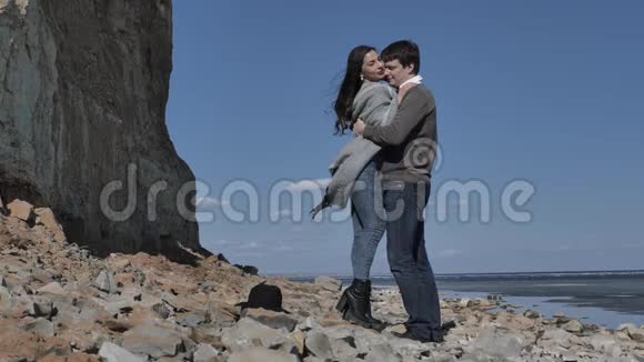 一对年轻夫妇走在岩石海岸上靠近一条冰封的河视频的预览图