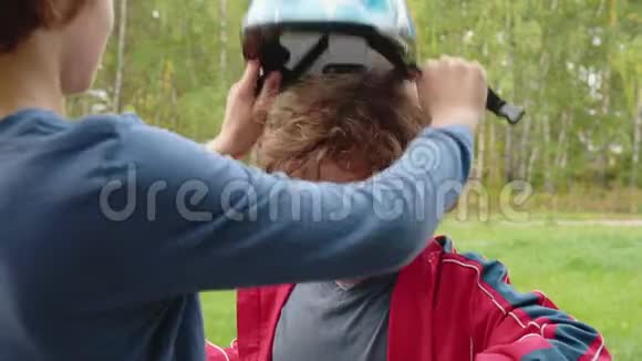 哥哥在夏天公园里把自行车头盔戴在弟弟的头上帮小男孩的大哥哥视频的预览图