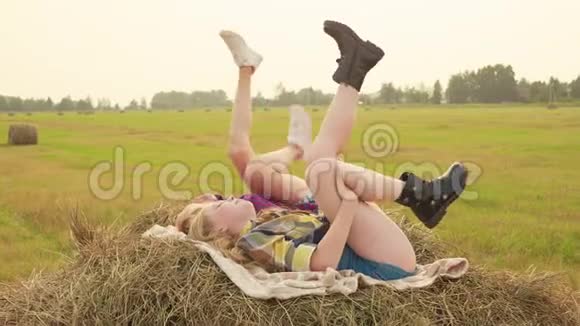 少女躺在干草堆和摇摆的腿上快乐的少年女孩在秋天的干草堆上移动双腿女朋友视频的预览图
