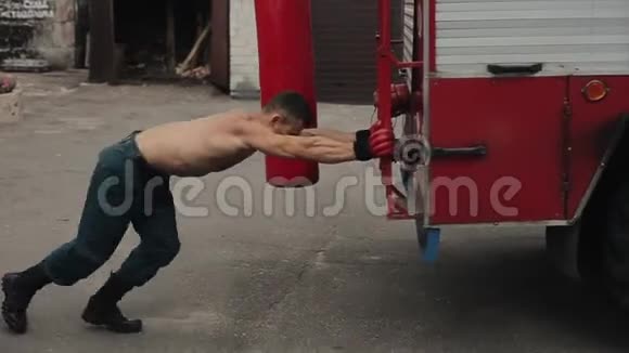 强壮的赤皮手套赤膊健美者试图推一辆大卡车背景中的红色沙袋视频的预览图