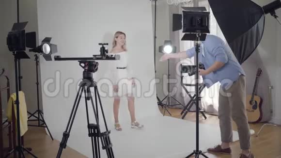 拍摄的后台摄影师和一个站在摄影棚白色背景上的模特女孩握手视频的预览图