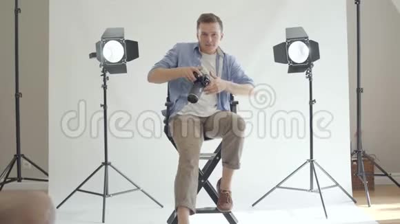 专业摄影师一边坐在椅子上看相机一边拍照白人摄影师视频的预览图