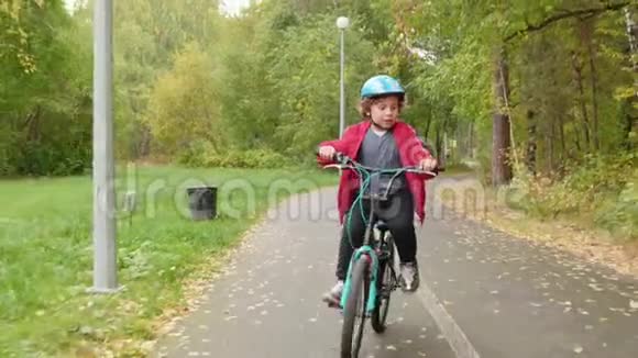快乐少年骑自行车在秋天公园骑自行车的男孩骑自行车前相机在城市公园少年男孩视频的预览图