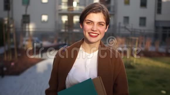 日落时一个年轻女人的肖像女孩穿着棕色外套手里拿着文件夹穿着视频的预览图