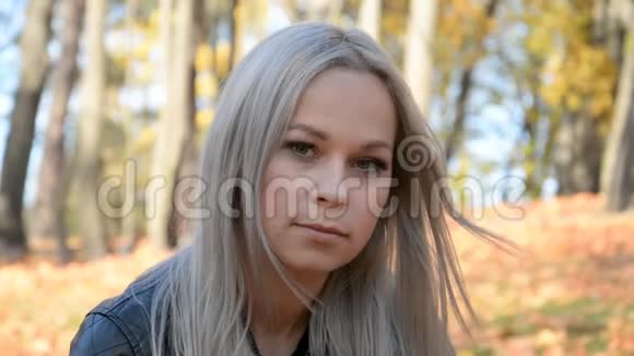 一位留着白发的美丽女孩的户外肖像落叶背景上带着悲伤的表情视频的预览图