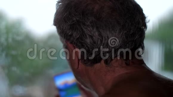 老人看着站在窗口的智能手机视频的预览图