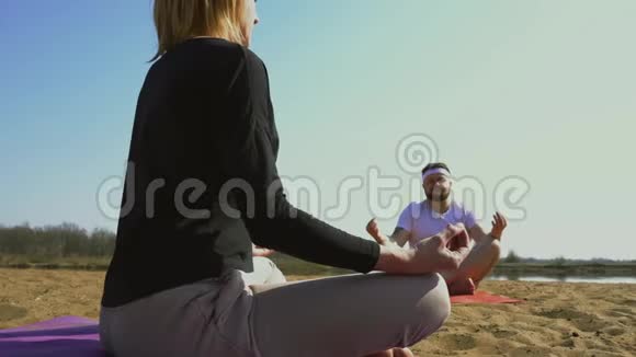 一个留着胡须的白种人男人和一个女人在练习瑜伽之前在河岸上沉思大自然健康视频的预览图