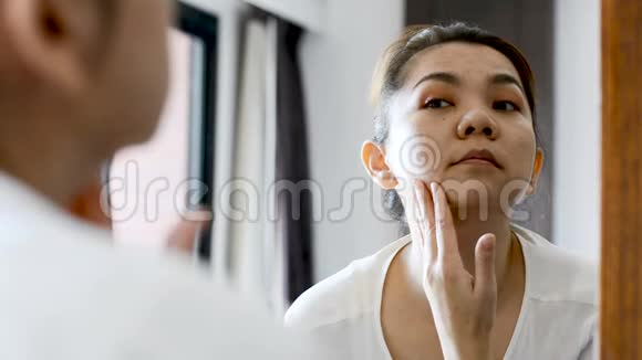 中年亚洲女人看着镜子里的皱纹和面部问题视频的预览图