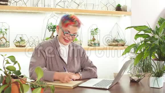 一位思想开放的商务女性戴着眼镜微笑着坐在桌上拿着笔记本电脑和笔记本电脑看一看视频的预览图