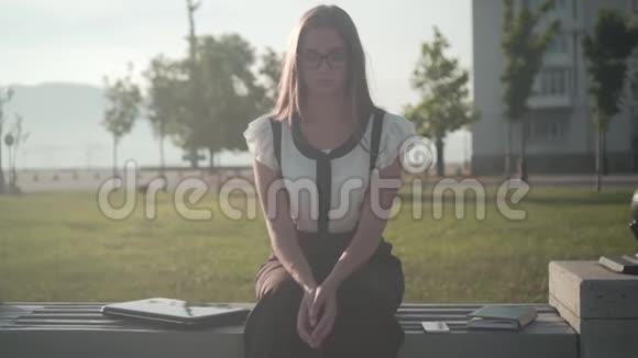 穿着白衬衫和眼镜坐在长凳上的女商人女孩累了她的脸特写不集中视频的预览图