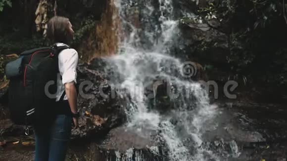 女孩背包客在雨林中享受瀑布视频的预览图