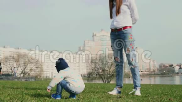 小男孩背对着镜头坐在草地上玩栗子和他年轻的妈妈视频的预览图