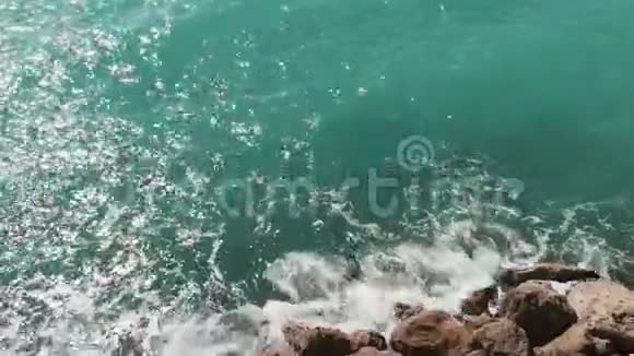 穿红色衣服的女人站在岩石悬崖上双手分开蓝色的水击打在岩石码头海滩上鸟瞰图视频的预览图