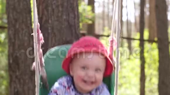 美丽的小男孩穿着红色的巴拿马脸上有蚊子叮咬快乐的微笑骑在秋千上视频的预览图