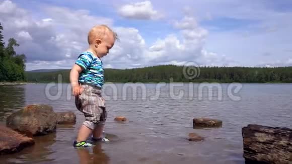 小男孩站在一个森林湖里玩着从湖底捡来的石头视频的预览图