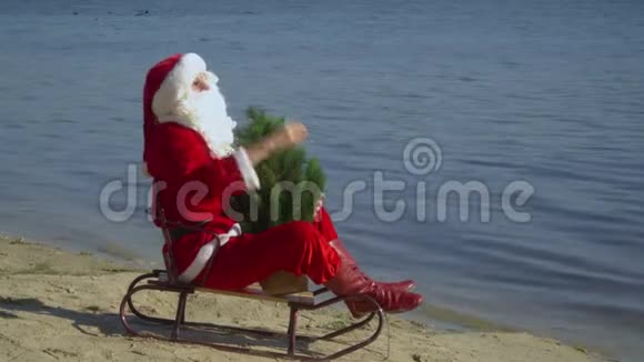 圣诞老人坐在沙滩上的雪橇上抱着一棵圣诞树望着远处圣诞老人视频的预览图