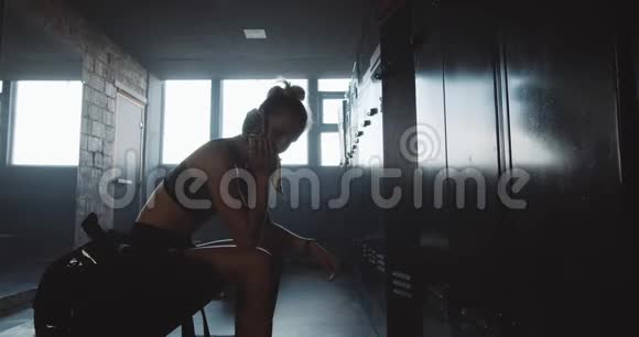 一个白人女子独自坐着离开黑暗的健身房更衣室在糟糕的一天缓慢的运动后感到不知所措视频的预览图