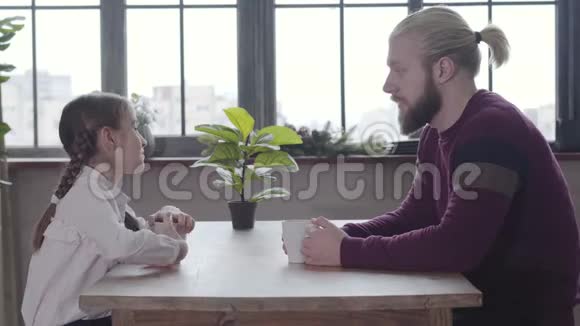 年轻的白种人男人和十几岁的女孩坐在桌子旁聊天父亲和女儿一起在视频的预览图