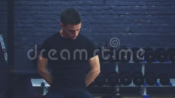 一个穿黑色T恤的运动小男孩坐在健身房里有运动身体的人在这段时间里他展示了视频的预览图