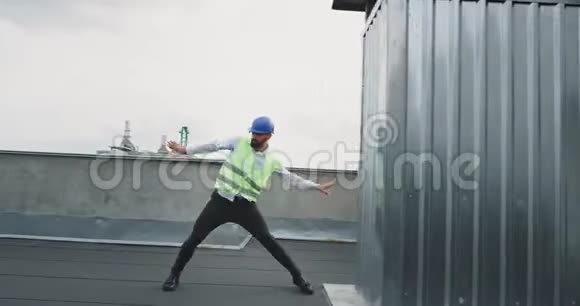 在施工现场跳舞一个有魅力的建筑工人或工程师戴着安全帽他在滑稽地移动视频的预览图