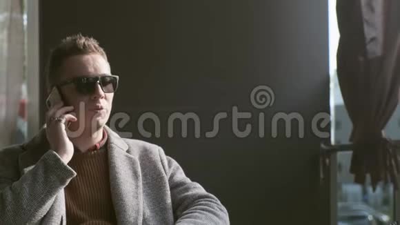 一个穿着外套和太阳镜的男人坐在咖啡馆里视频的预览图