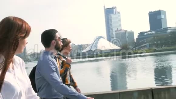 年轻漂亮的女人和三个男人正在沿着城市的堤坝走背景是高楼大厦视频的预览图