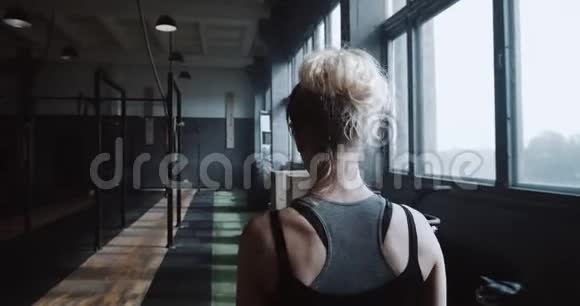 镜头跟随着年轻的金发女运动员独自在空荡荡的大体育馆里散步准备做慢动作视频的预览图