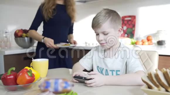 儿子玩手机妈妈为儿子准备三明治家庭幸福视频的预览图